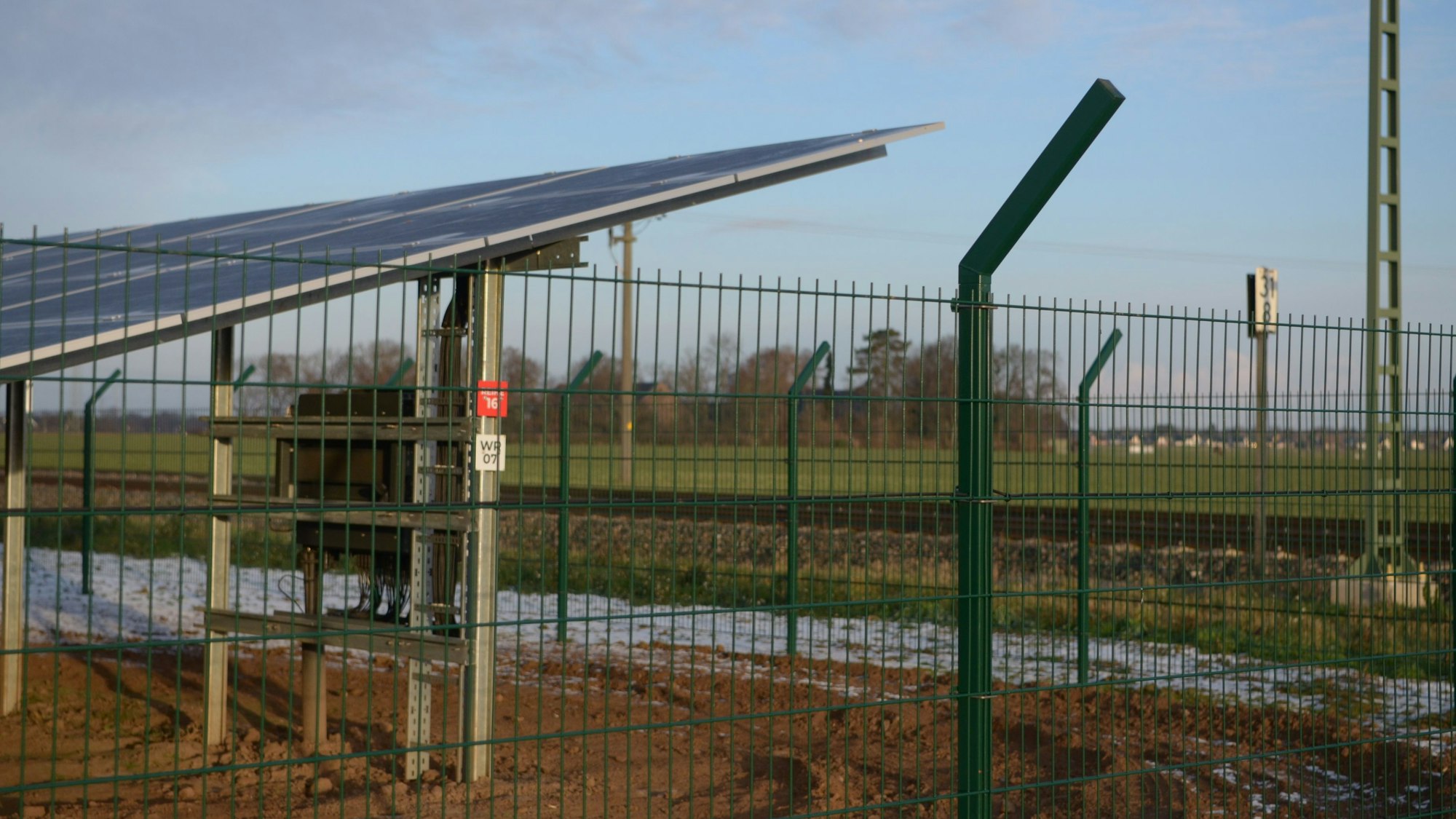 Ein Solarmodul hinter einem Zaun ist zu erkennen, dahinter der Ratsheimer Hof bei Kuchenheim.