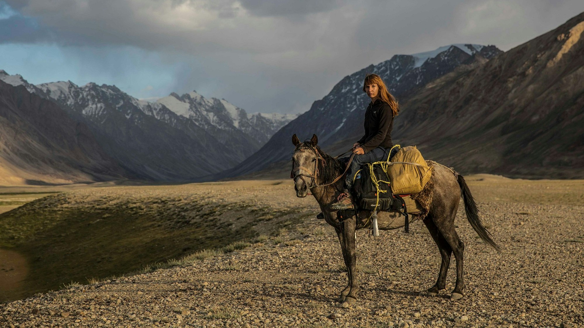 Priska Seisenbacher auf dem Rücken eines Pferdes im Gebirge.