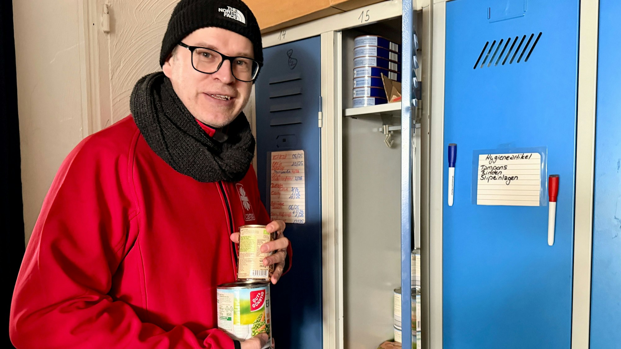 Markus Niederstein steht vor einem der geöffneten Spinde und holt Konservendosen heraus. Auf den Türen der blauen Schränke hängen Listen, auf denen der Bestand festgehalten wird.