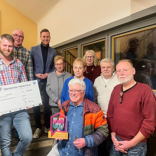 Neun Menschen haben sich zum Gruppenbild versammelt. Ein Mann hält einen überdimensionalen Scheck in den Händen, ein anderer einen Preis.