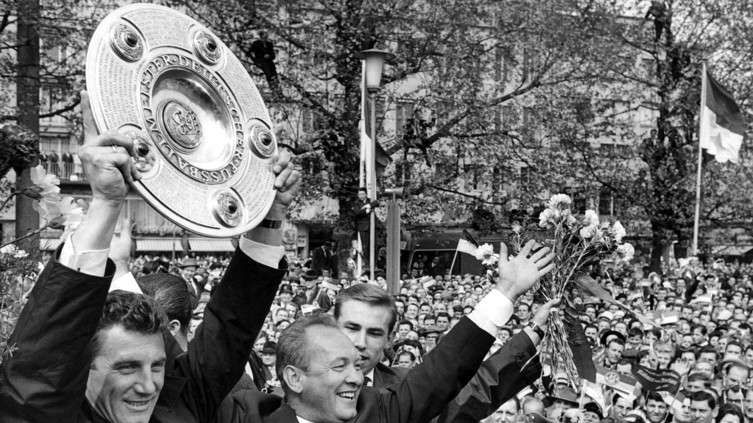 Kapitän Hans Schäfer vom 1. FC Köln (l) jubelt mit der Meisterschale über den Gewinn der Deutschen Fußball-Meisterschaft beim Empfang in der Kölner Innenstadt. Neben ihm jubeln Trainer Zlatko „Tschik“ Cajkovski (2.v.l.) und Fritz Pott (Archivfoto vom 13.05.1962).