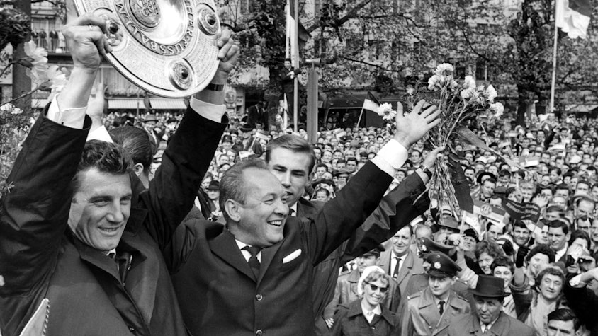 Kapitän Hans Schäfer vom 1. FC Köln (l) jubelt mit der Meisterschale über den Gewinn der Deutschen Fußball-Meisterschaft beim Empfang in der Kölner Innenstadt. Neben ihm jubeln Trainer Zlatko „Tschik“ Cajkovski (2.v.l.) und Fritz Pott (Archivfoto vom 13.05.1962).