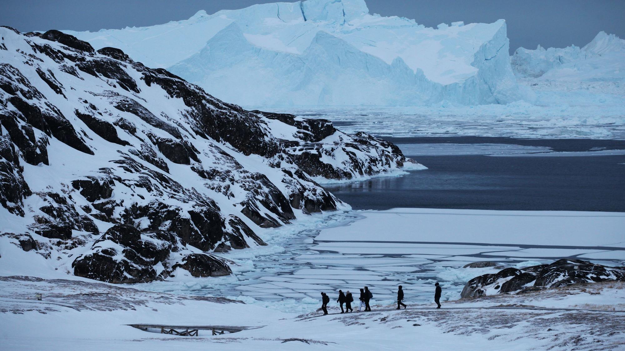 Eine Gruppe Touristen wandert in der Nähe des grönländischen Ortes Ilulissat vor der Kulisse riesiger Eisberge entlang.
