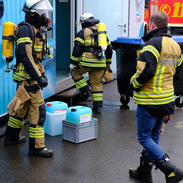 Drei Feuerwehrleute - zwei mit Atemschutz - haben Kanister mit einer Chlorgasflüssigkeit aus einem blauen Schwimmcontainer geborgen.
