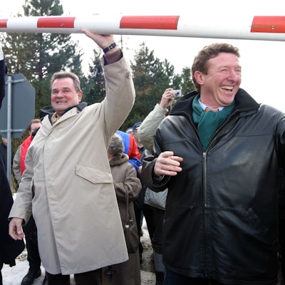 Ralf Hergarten, Günter Rosenke und Manfred Poth heben den Schlagbaum über ihre Köpfe.Im Hintergrund sind andere Menschen zu sehen.