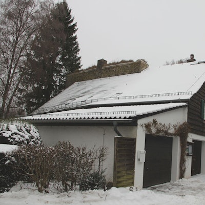 Nahe eines Tors des Burgberings in Kronenburg befindet sich ein Haus, an das eine Garage angebaut ist. Auf den Dächern liegt Schnee.