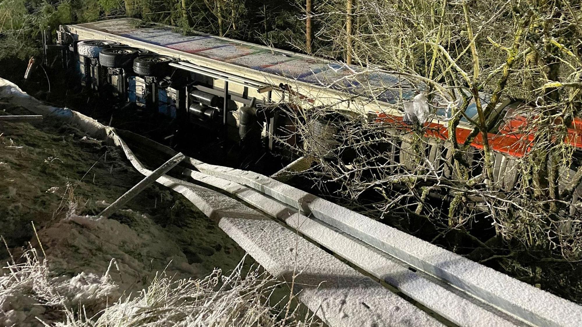Der Lkw liegt jenseits einer Leitplanke umgekippt in einem Abhang.