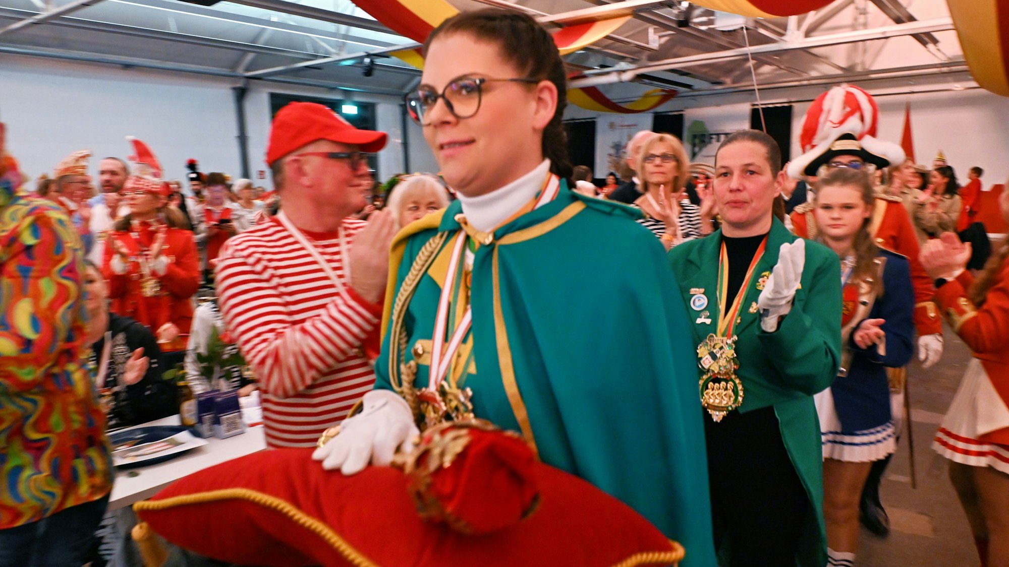 Adjutantin Patricia Flinn trägt das Narrenzepter, das auf einem roten Kissen aus Samt liegt, durch den voll besetzten Saal.