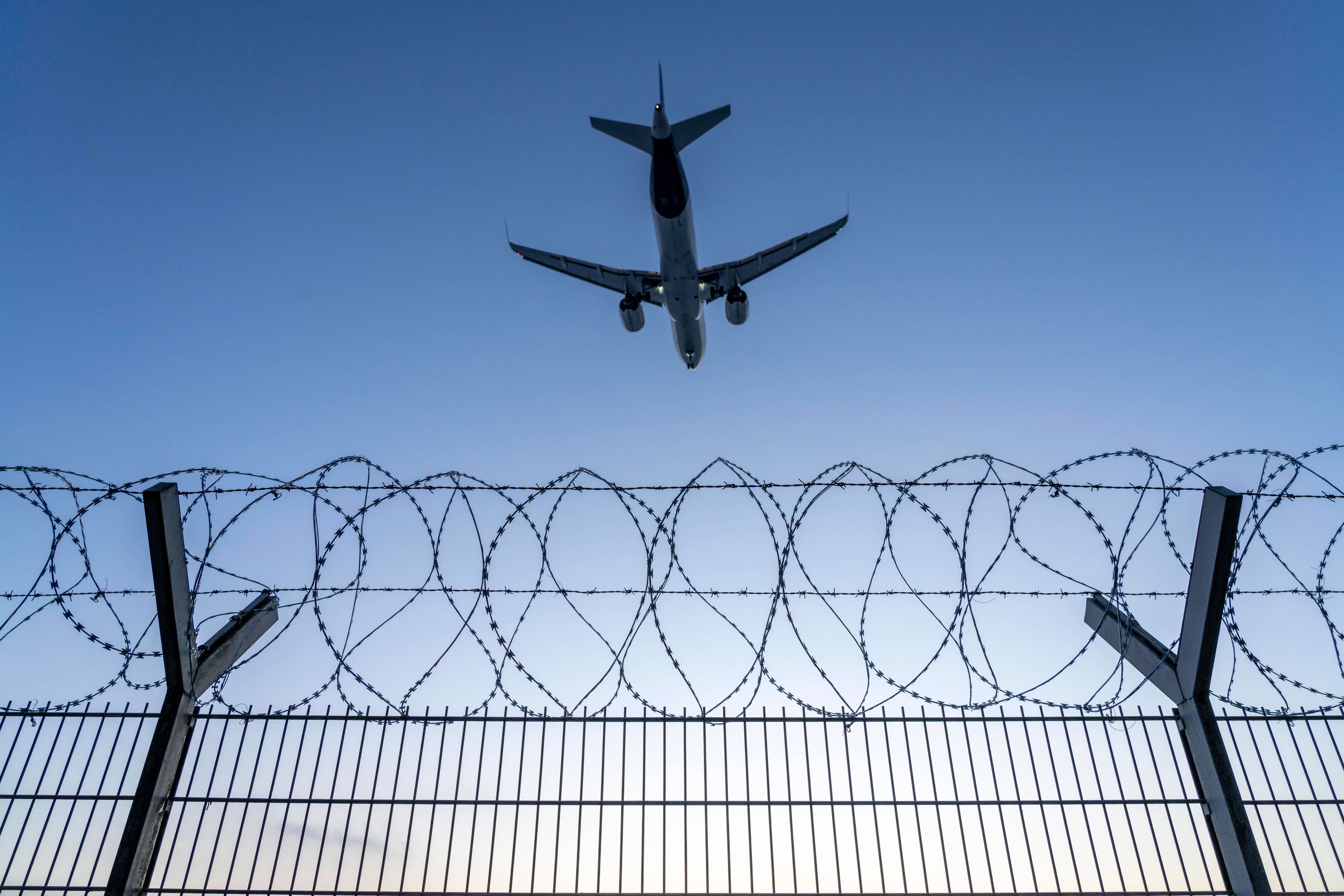 Symbolbild Sicherheit auf dem Flughafen, äußerer Zaun am Airport Düsseldorf International, Stahldrahtzaun, mit S-Draht Rollen, NATO-Draht, auf der Zaunkrone, Flugzeug im Landeanflug, Sonnenuntergang, NRW, Deutschland, Sicherheit Flughafen *** Symbolic image security at the airport, outer fence at Düsseldorf International Airport, steel wire fence, with S wire rolls, NATO wire, on the fence top, airplane approaching, sunset, NRW, Germany, airport security