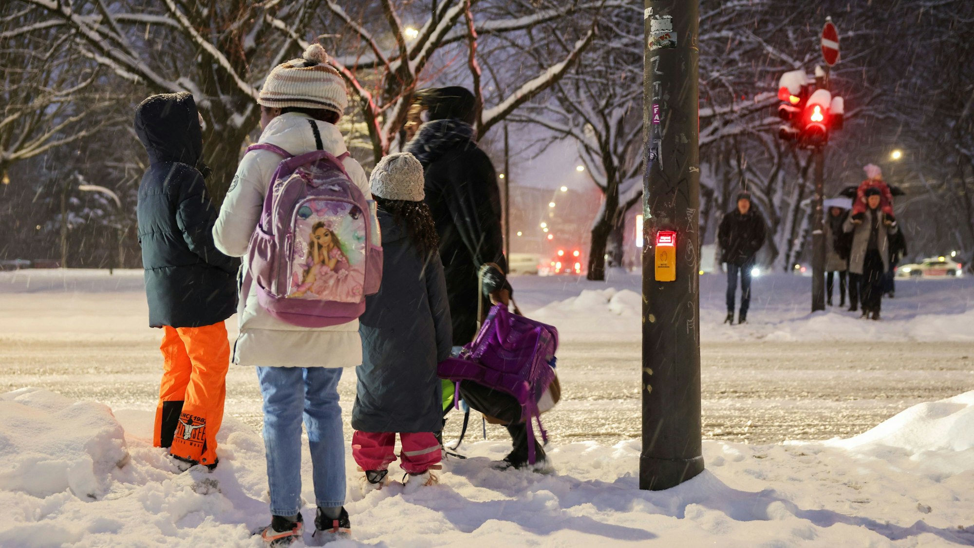 Eine Mutter trägt die Schulranzen ihrer Kinder während sie im Schnee an einer Fußgängerampel.