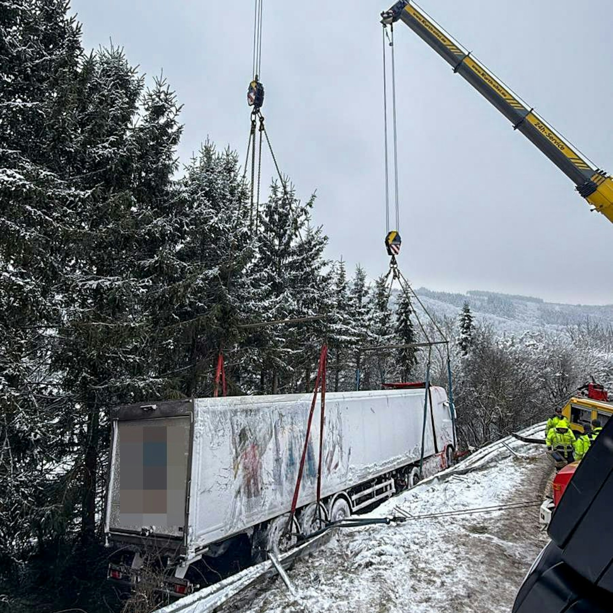 Mithilfe zweier Krane wird ein in einen Abhang gekippter Lastzug geborgen.