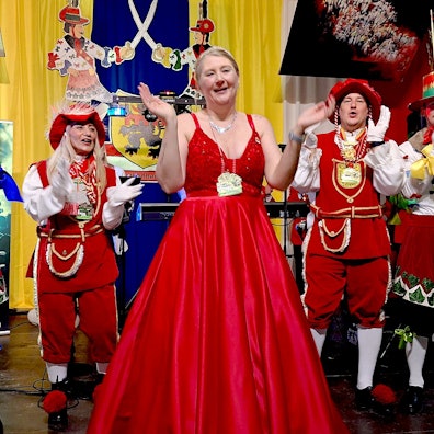 Eva Walber steht in der Mitte in einem roten Kleid, umgeben von Männern und Frauen in roten Kostümen.