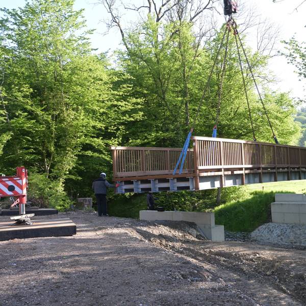 Eine Brücke wird mit einem Kran auf zwei Stützpfeiler gehoben.
