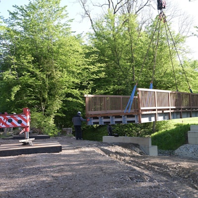 Eine Brücke wird mit einem Kran auf zwei Stützpfeiler gehoben.