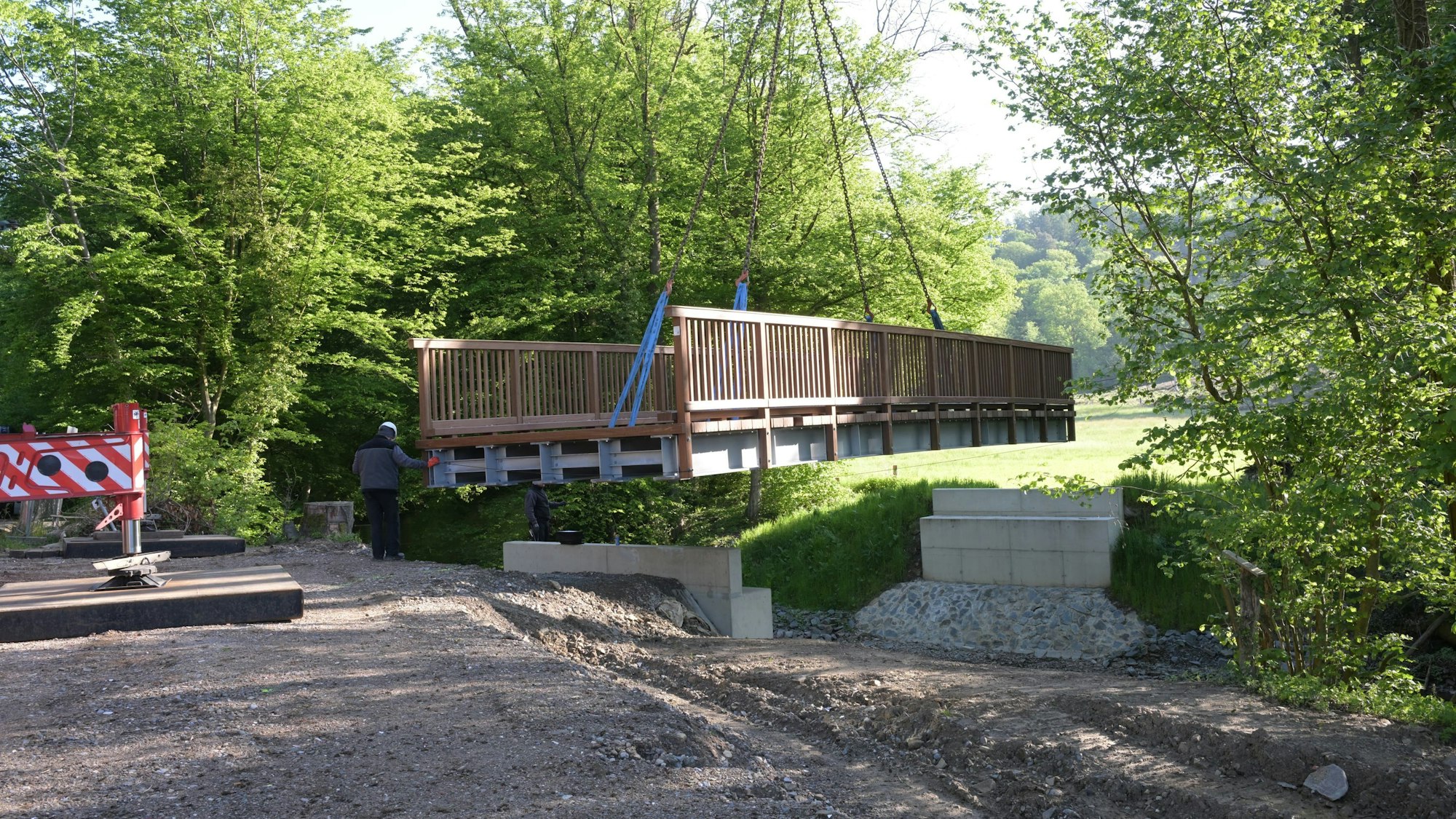 Eine Brücke wird mit einem Kran auf zwei Stützpfeiler gehoben.