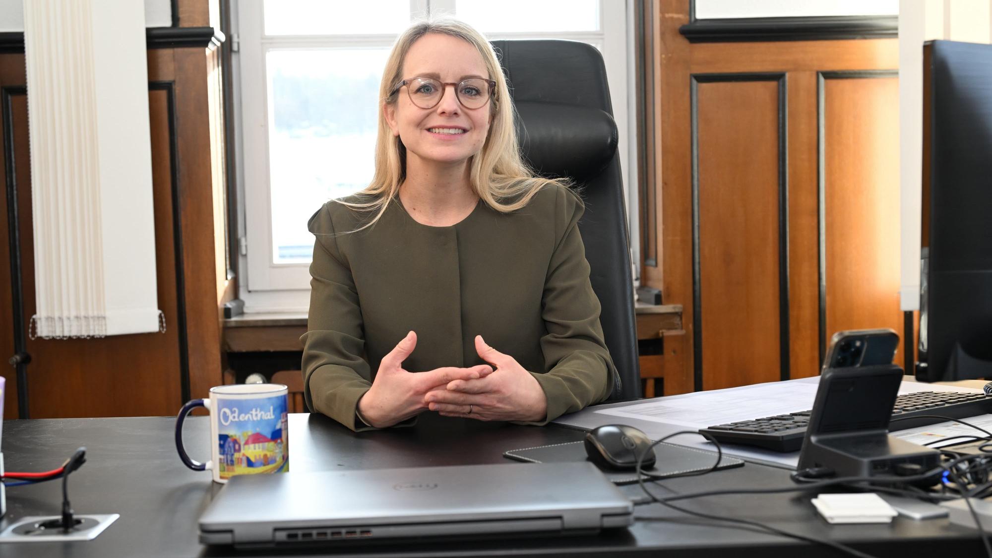 Eine Frau mit blondem, langen Haar und Brille sitzt an einem Schreibtisch.