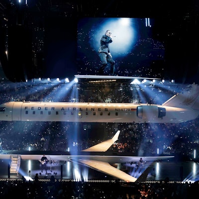 Apache 207 steht auf der Bühne der Lanxess-Arena. In der Mitte der Bühne steht ein Privatjet, der der Länge nach geteilt ist.