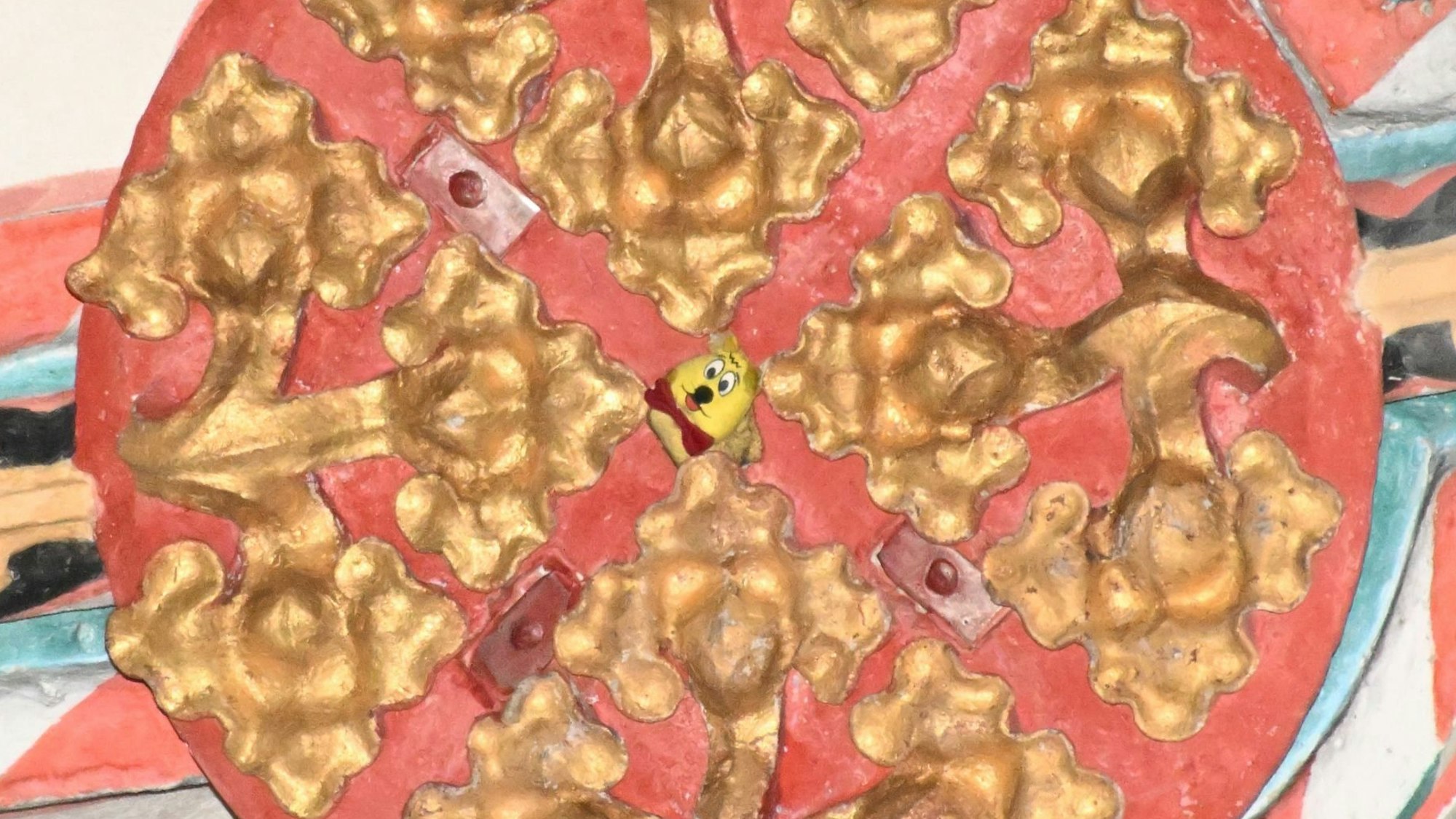 Der Schlussstein in einem gotischen Kreuzrippengewölbe. In der Mitte schaut ein Tütchen mit Gummibärchen hervor.