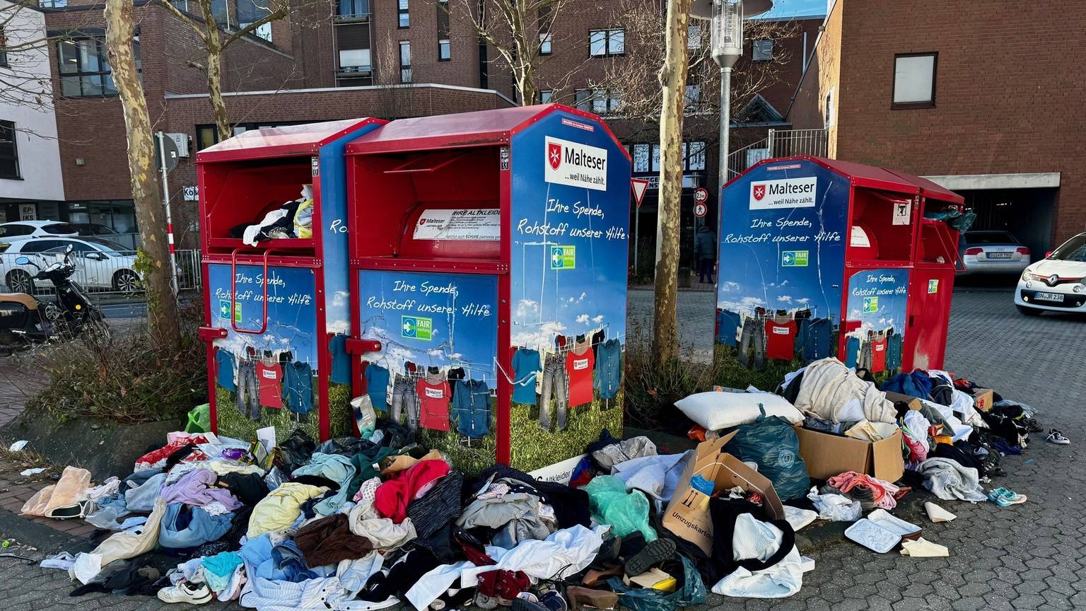 Kleider und Müll liegen verstreut vor vollen Altkleidercontainern.