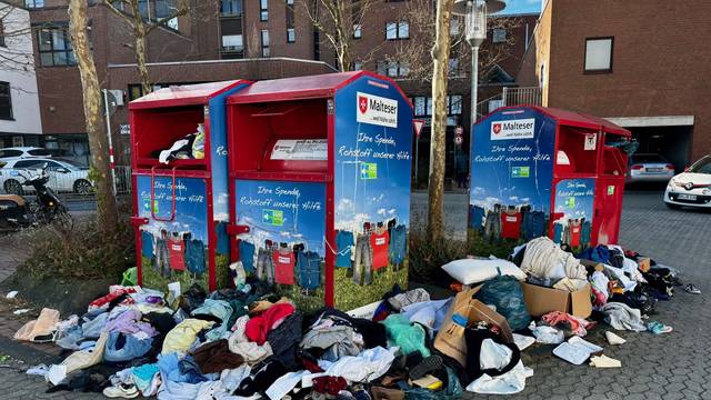 Kleider und Müll liegen verstreut vor vollen Altkleidercontainern.