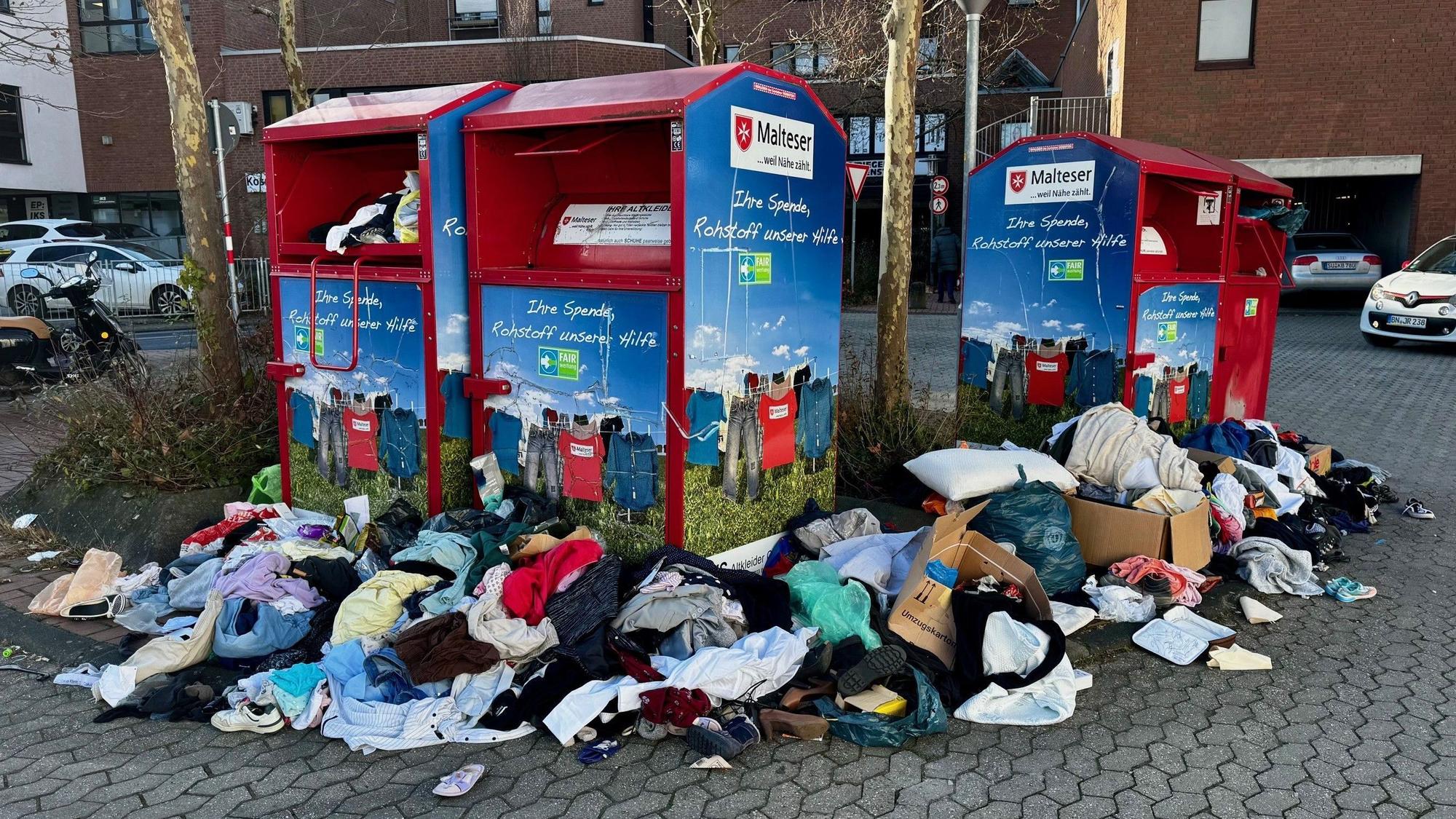 Kleider und Müll liegen verstreut vor vollen Altkleidercontainern.