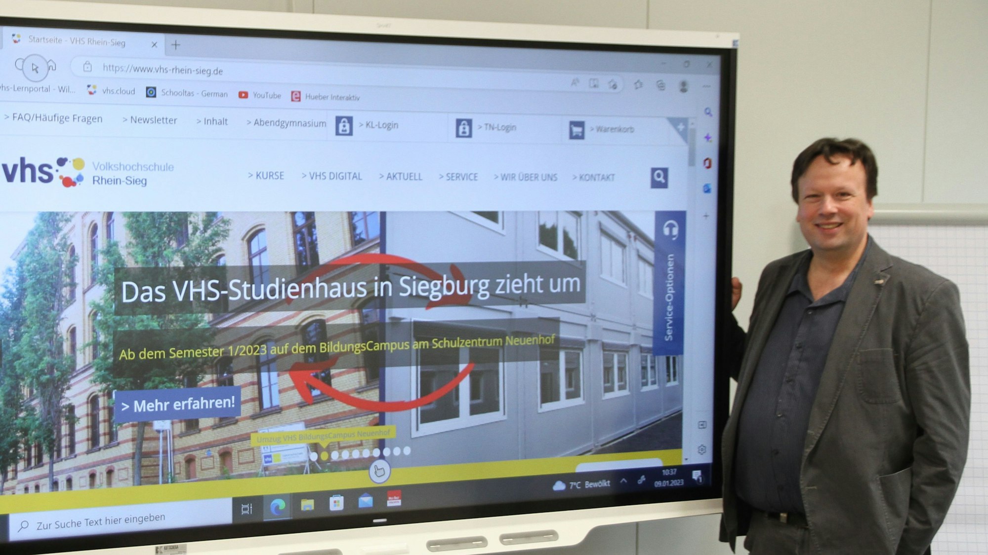 Ein Mann steht neben einem großen Computerbildschirm in einem Unterrichtsraum.