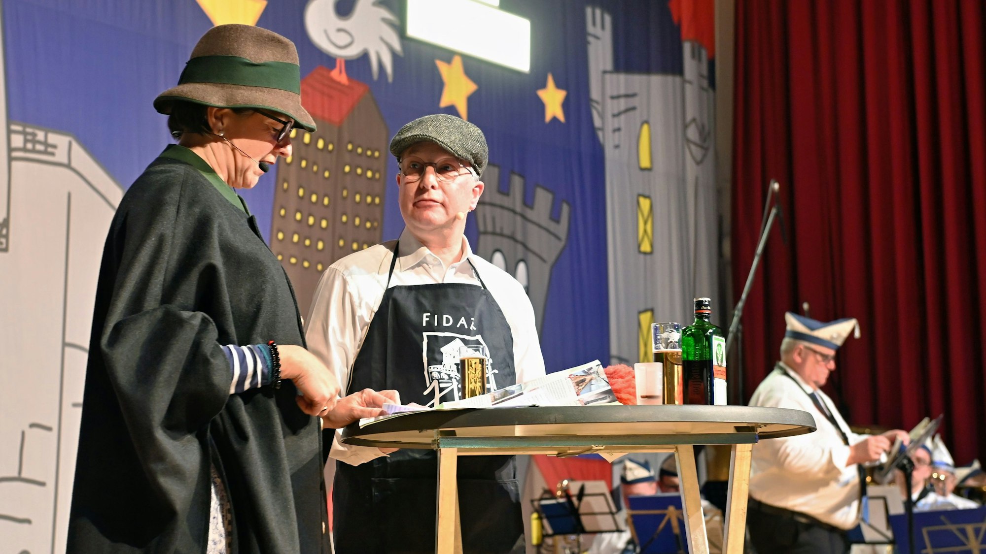 Fritz und Marianne Komp stehen als „Kinz und Hunz" kostümiert an einem Tisch, im Hintergrund sind uniformierte Karnevalisten zu sehen.