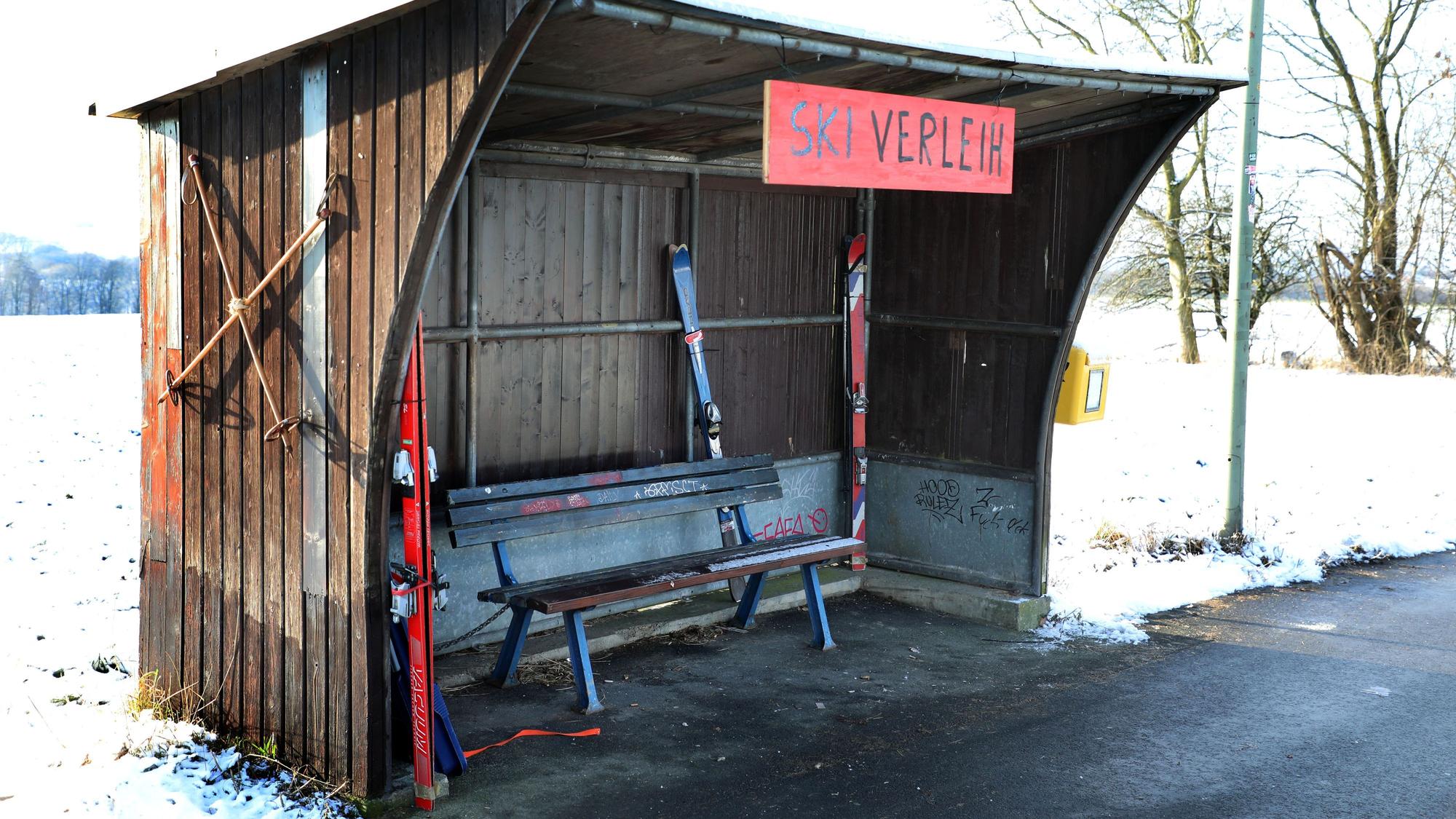 In einem Buswartehäuschen in Rösrath-Stöckchen stehen Ski und ein Rodelbob, ein Schild trägt die Aufschrift „Ski-Verleih“.
