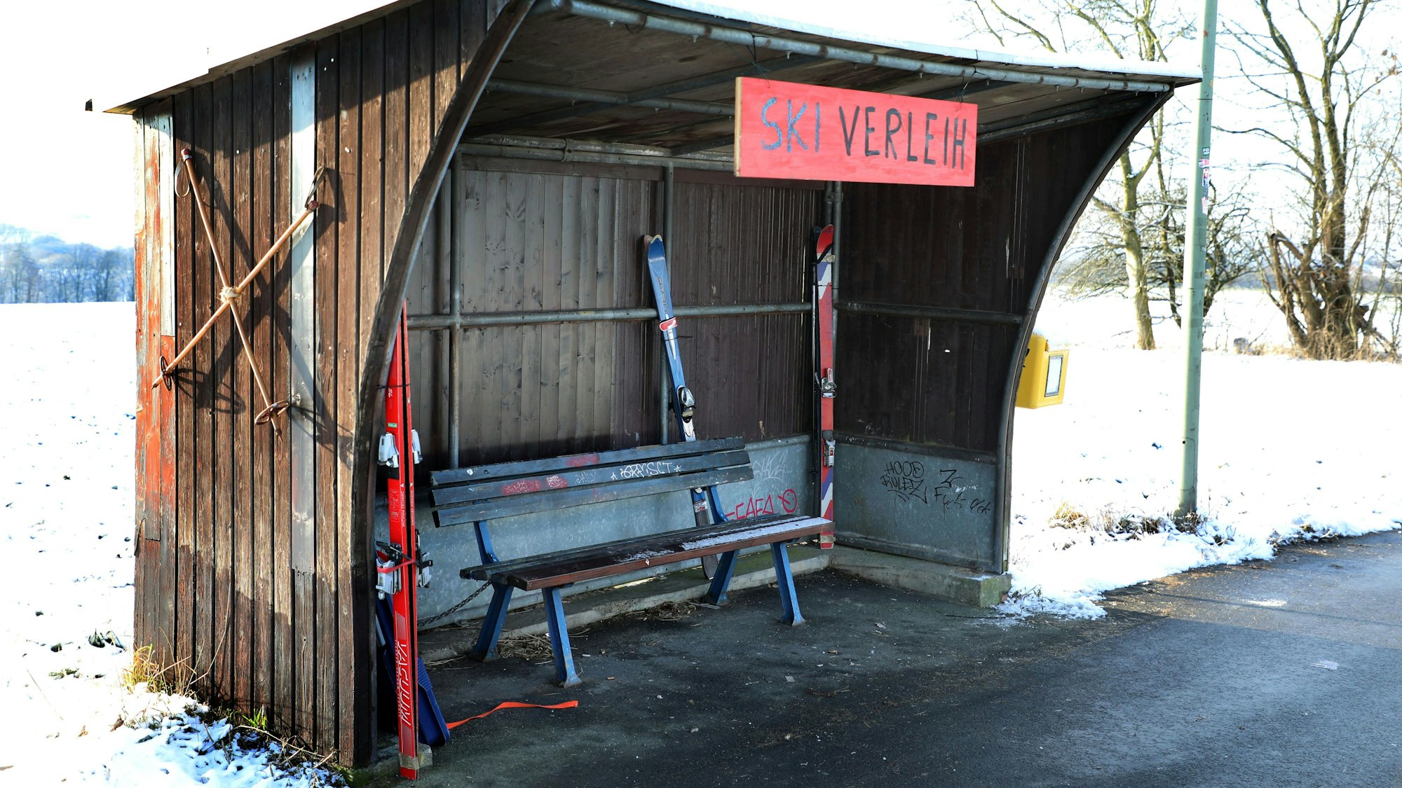 In einem Buswartehäuschen in Rösrath-Stöckchen stehen Ski und ein Rodelbob, ein Schild trägt die Aufschrift „Ski-Verleih“.