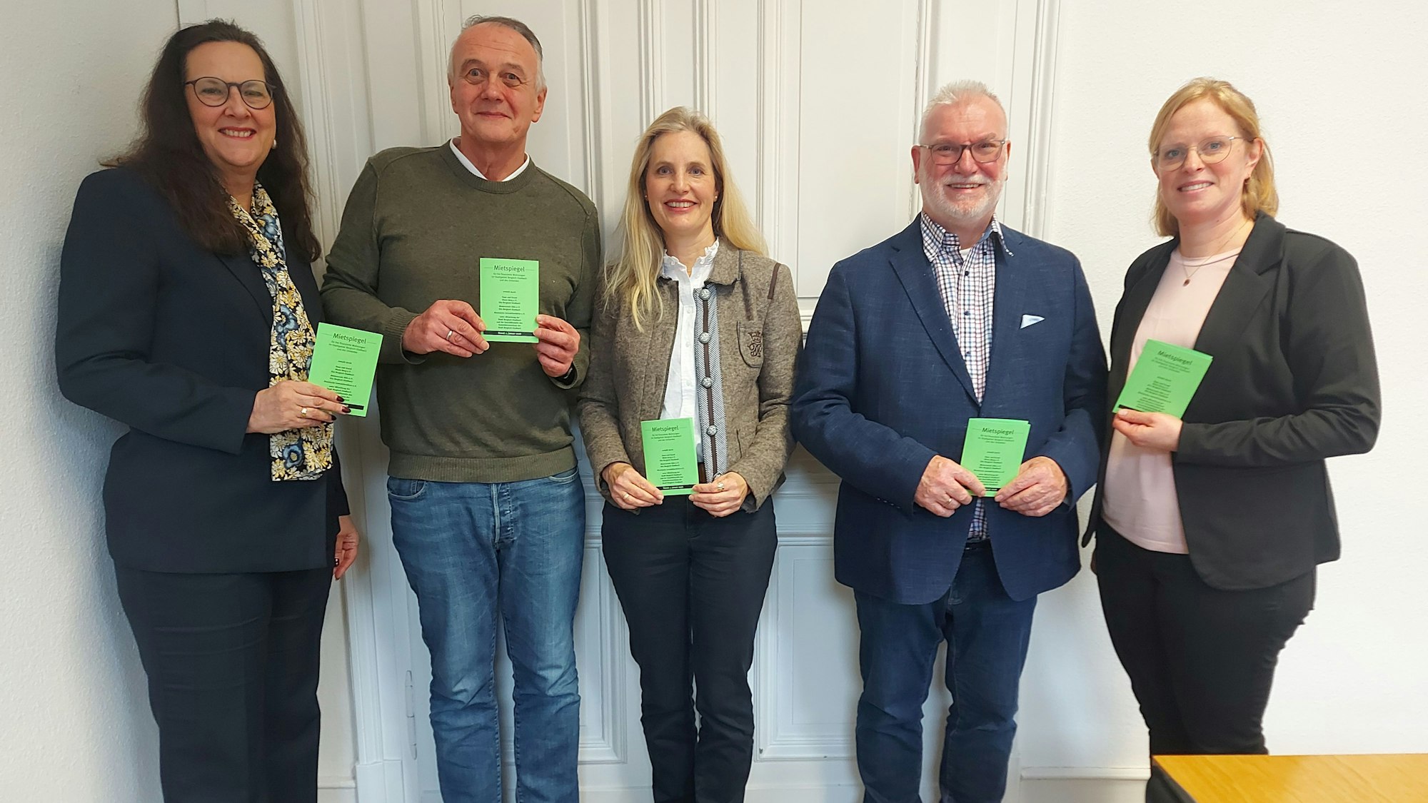 Drei Frauen und zwei Männer halten ein kleines grünes Heftchen in den Händen.