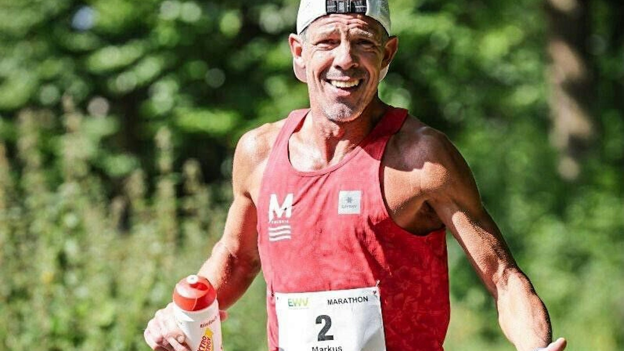 Markus Mey trägt beim Laufen eine Kappe mit dem Schirm nach hinten und hält in einer Hand eine Trinkflasche.