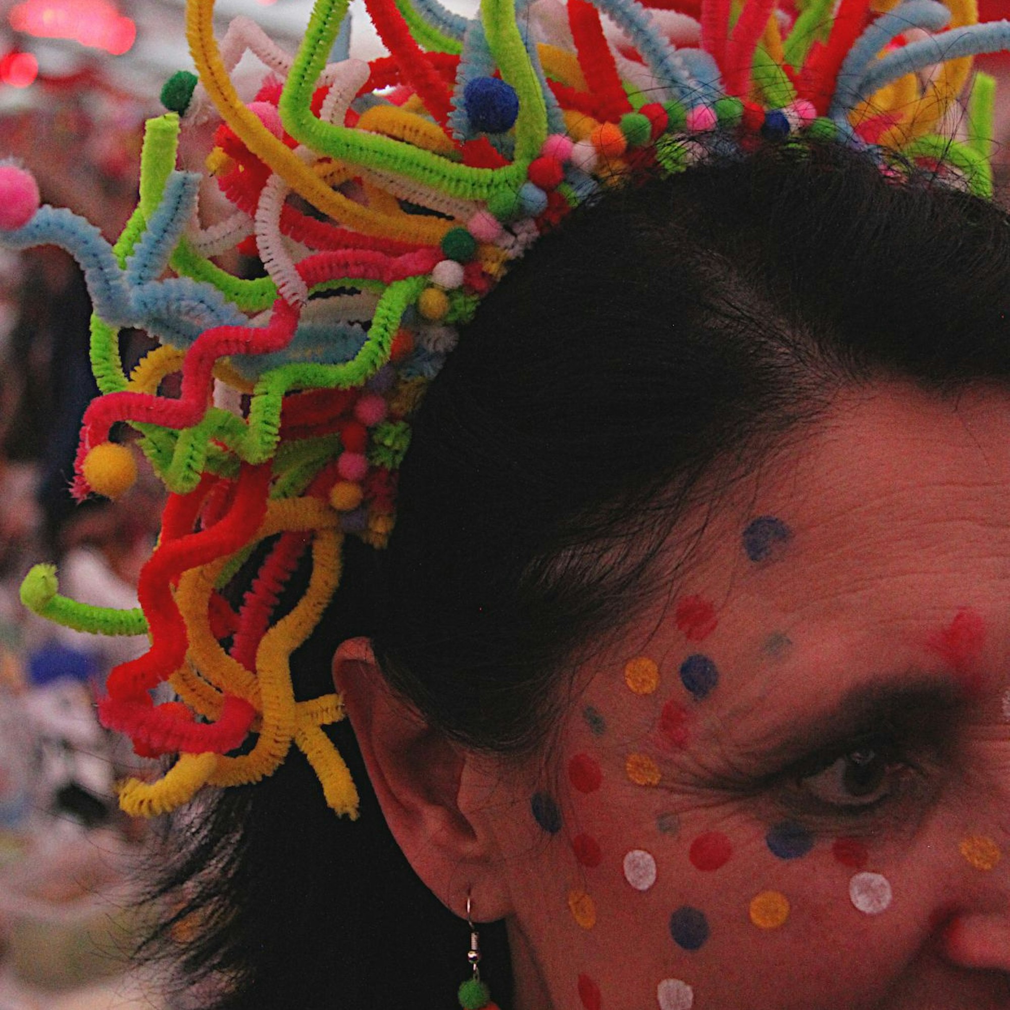 Das Bild zeigt eine Frau, die sich Konfetti ins Gesicht geschminkt hat. In den Haaren trägt sie Pfeifenreiniger.