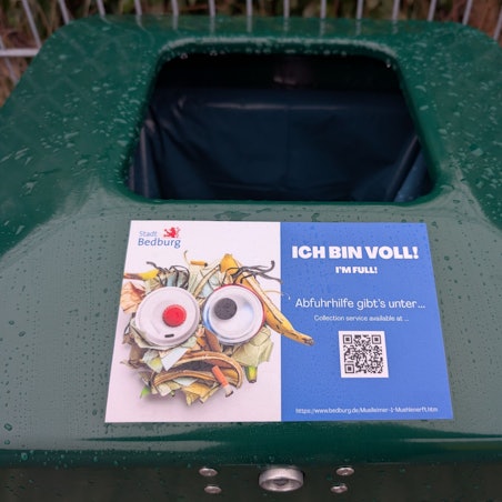 Zu sehen ist ein Aufkleber auf einem öffentlichen Mülleimer.