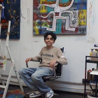 Ein Teenager sitzt auf einem Bürostuhl in einer Maler-Werkstatt.