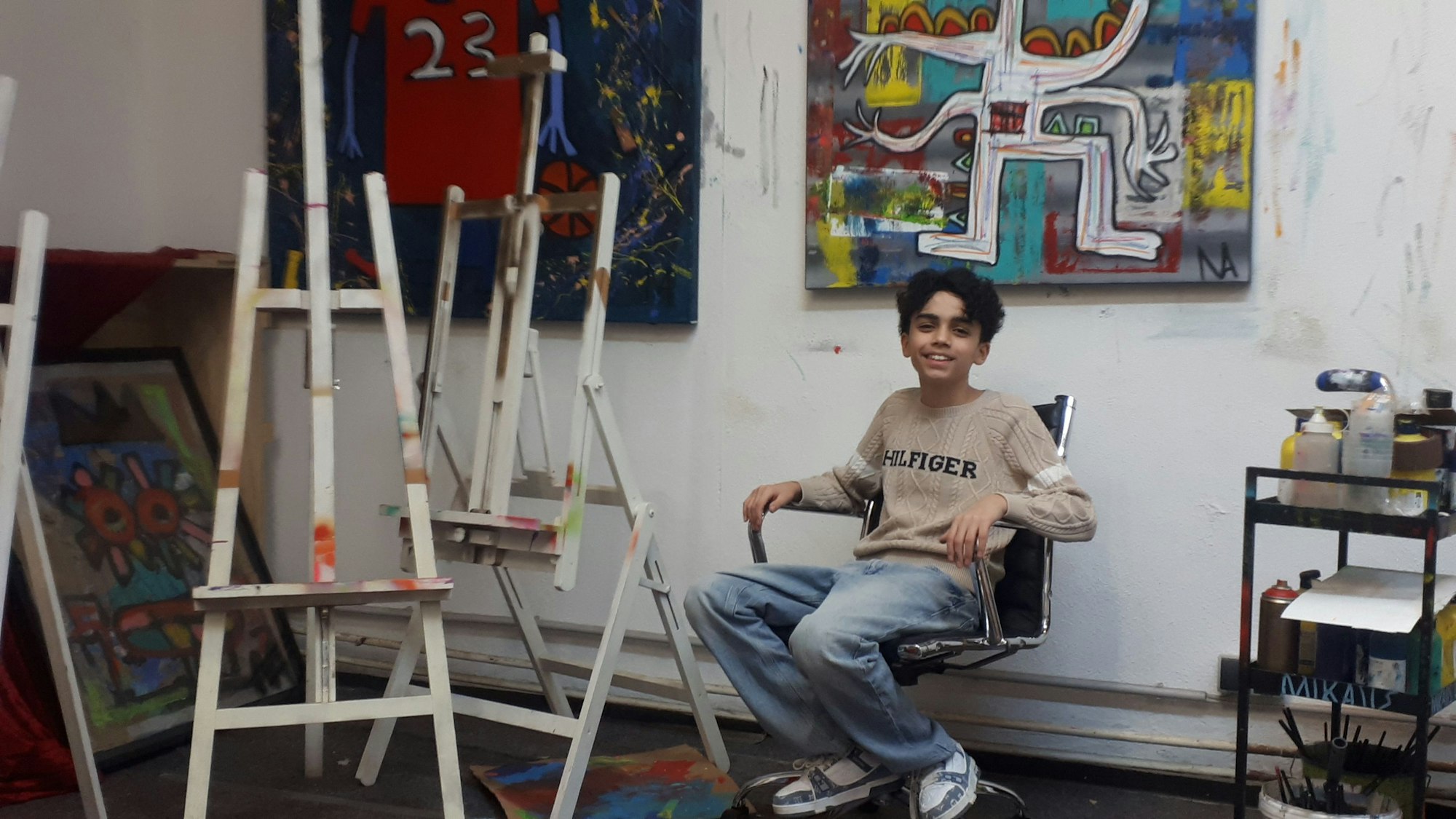 Ein Teenager sitzt auf einem Bürostuhl in einer Maler-Werkstatt.