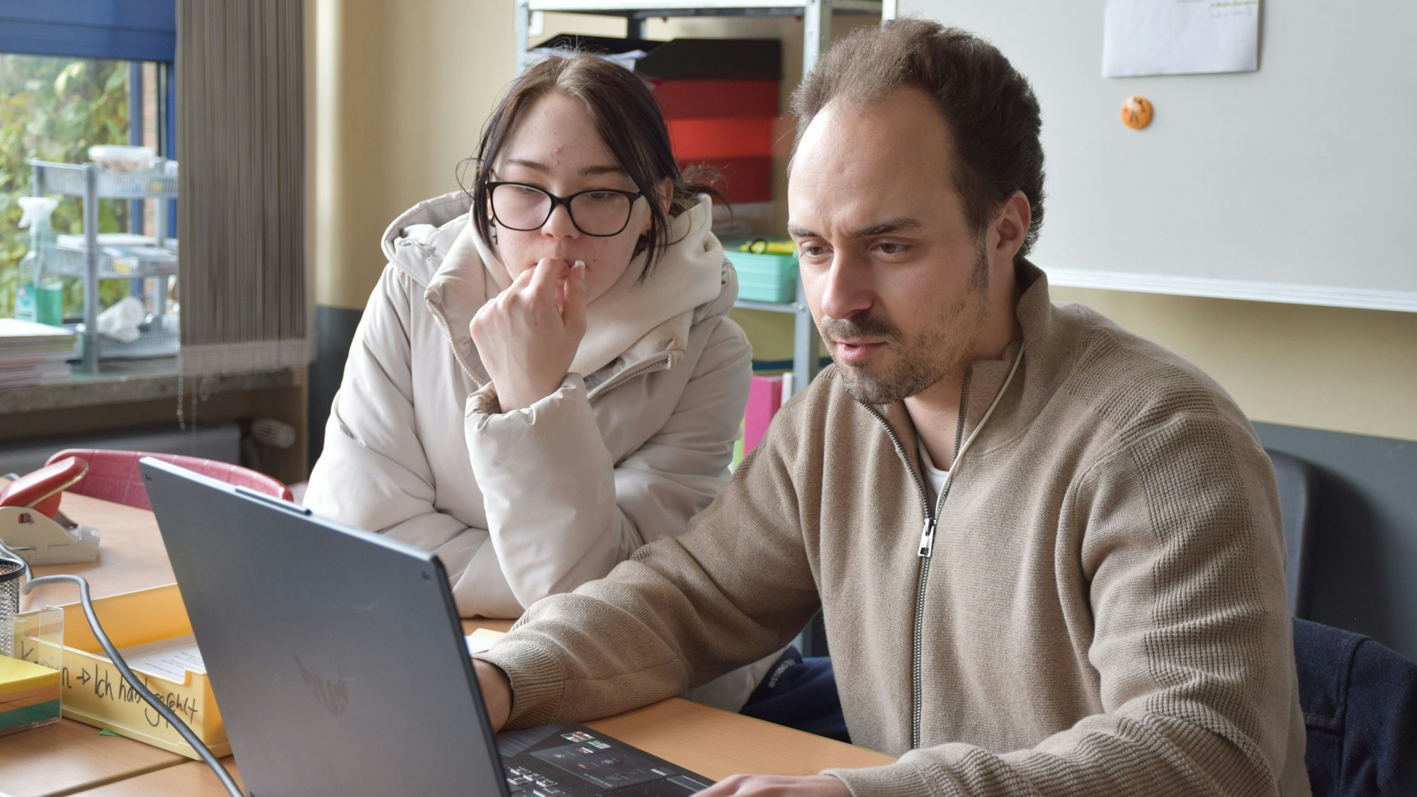 Felix Müller zeigt einer Schülerin etwas auf einem Laptop.