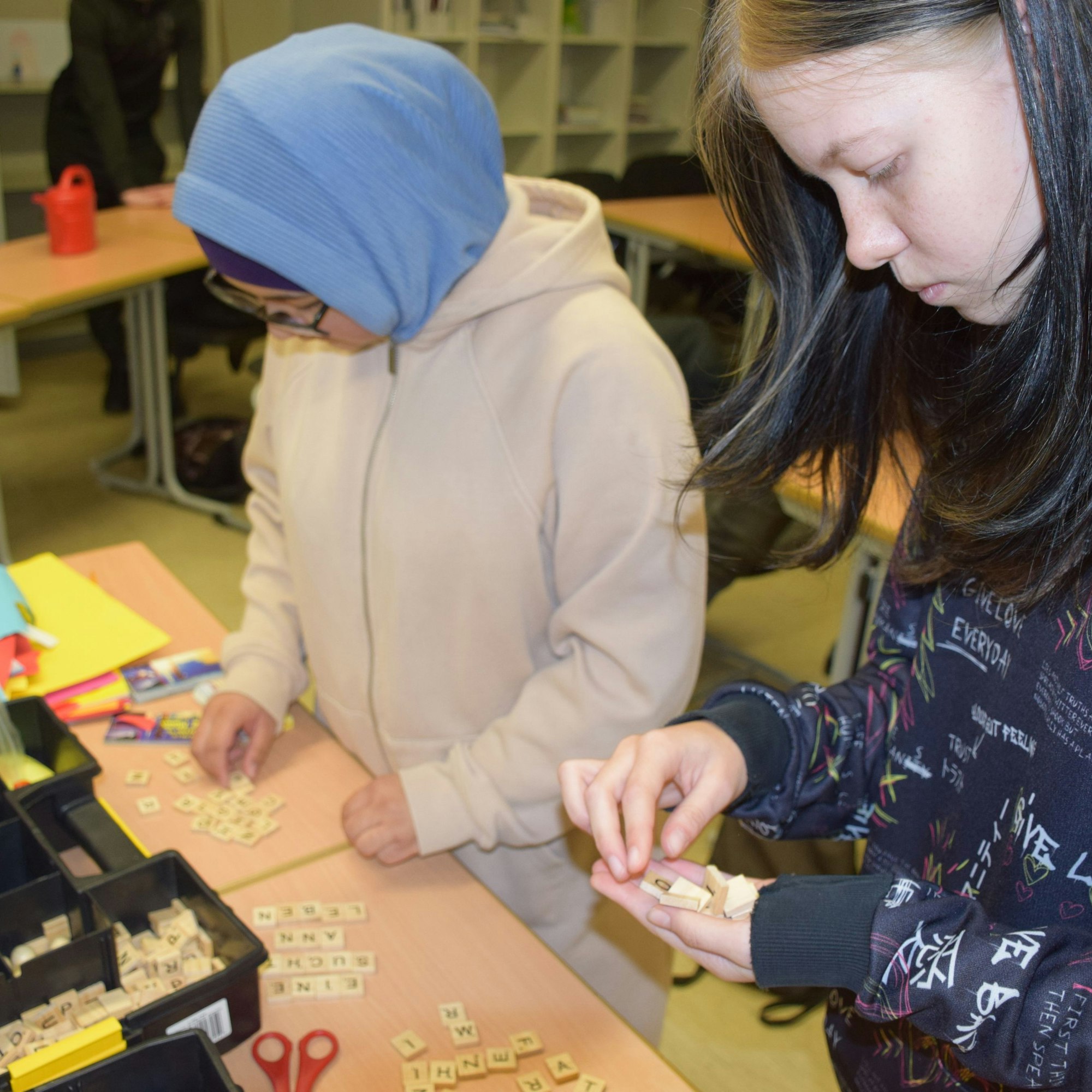 Zwei Mädchen legen Buchstaben für eine Bildgeschichte auf einen Tisch.