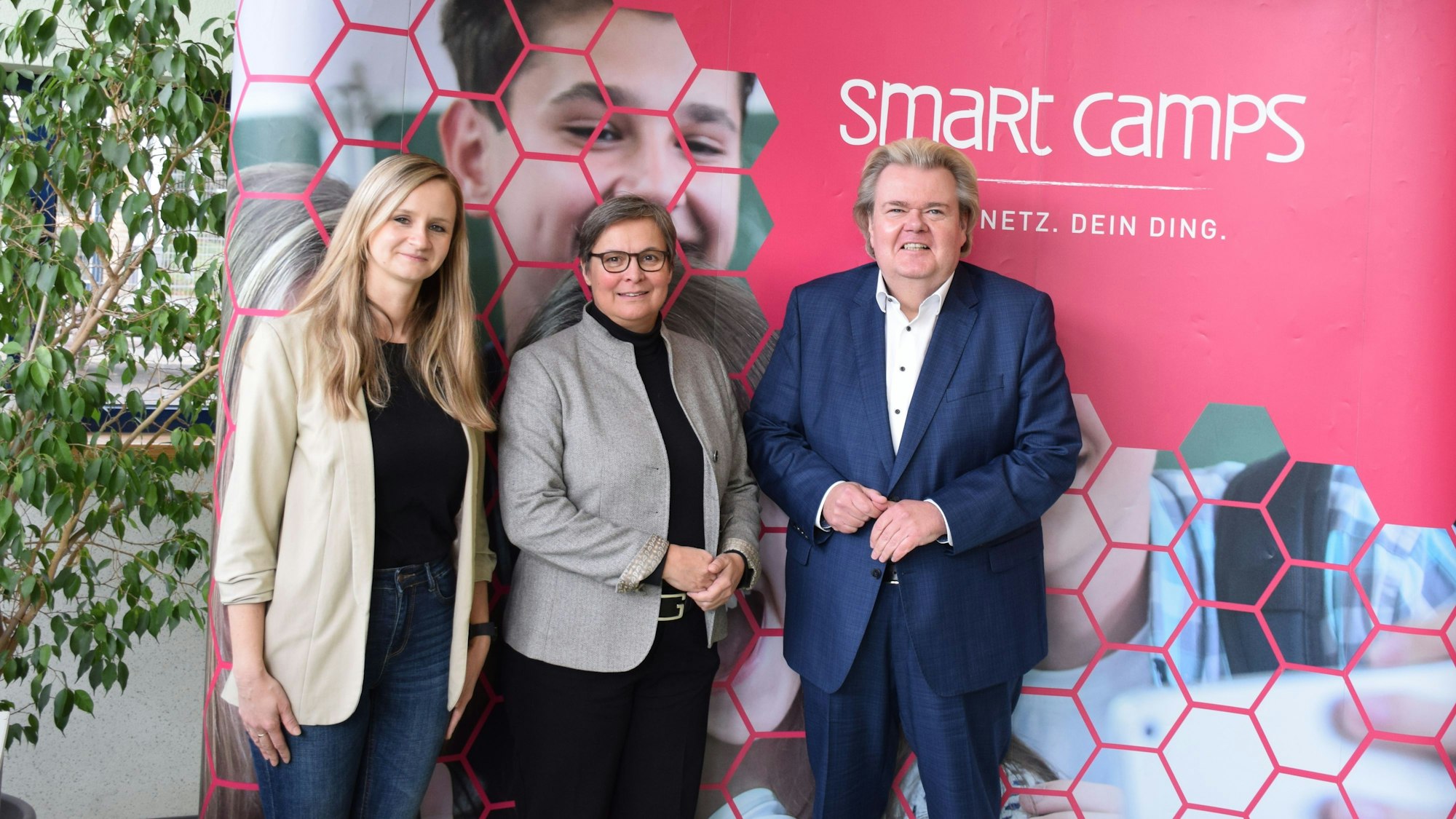 Die Obengenannten stehen vor einem Banner, auf dem „Smart Camps steht“.