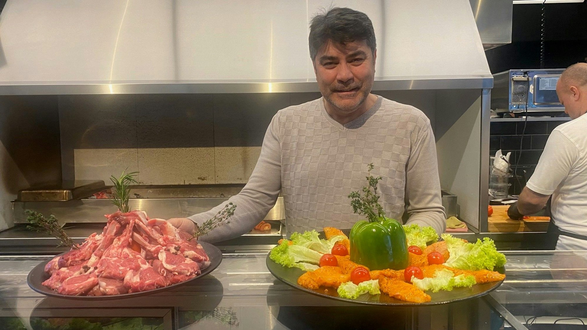 Zu sehen ist Osman Türkan, der große Teller mit Speisen in den Händen hält.