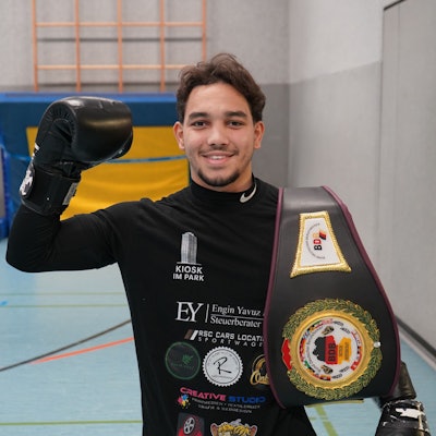 Kebdani hält eine behandschuhte Faust hoch, an seiner Schulter sein Gürtel.