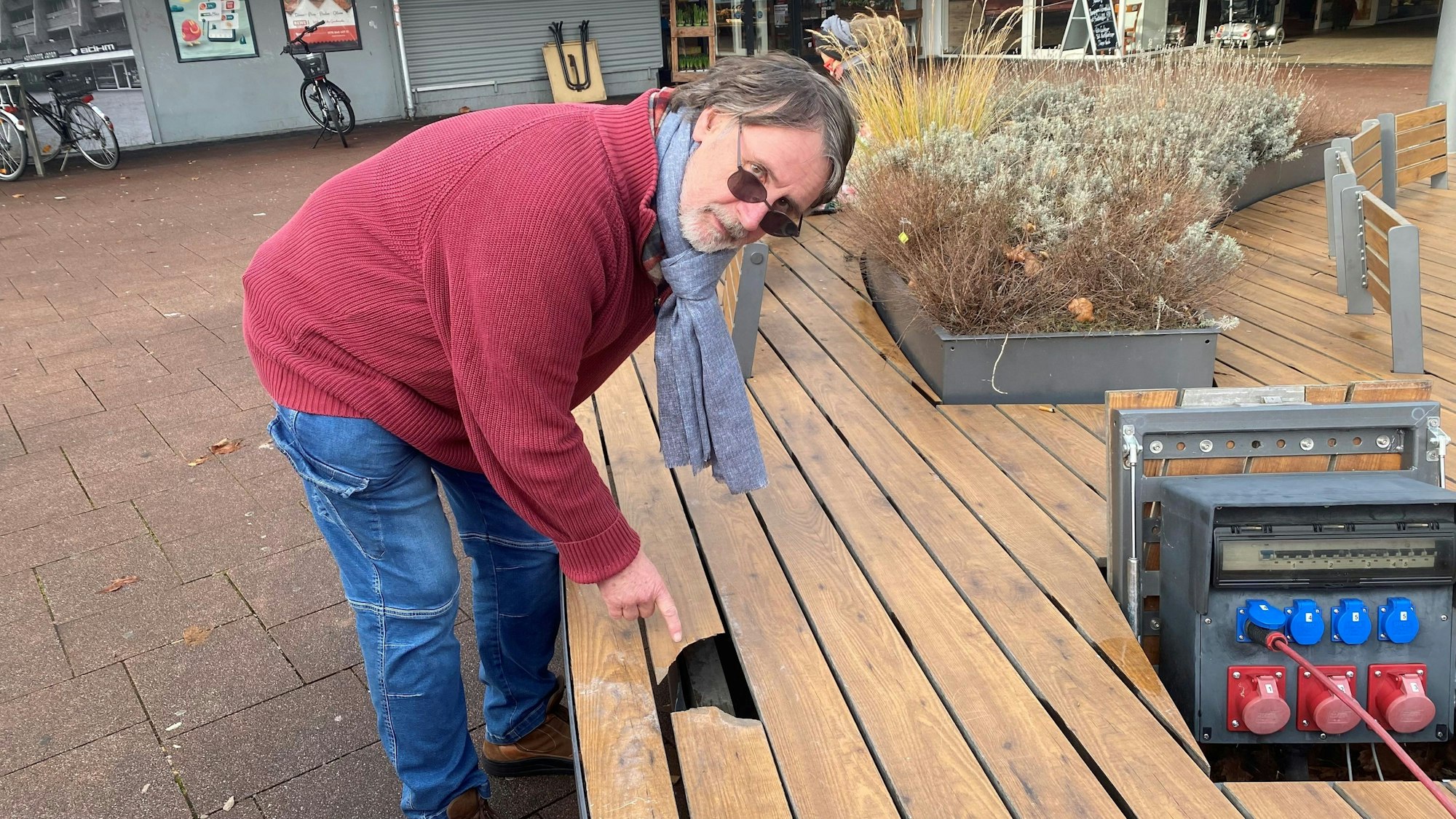 Zu sehen ist ein Mann, der auf ein Loch in einer Sitzbank zeigt.