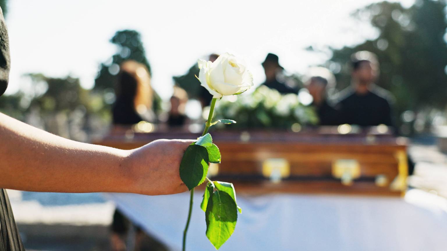 Eine Frau legt zum Andenken an eine verstorbene Person eine Blume auf einem Sarg ab. (Symbolfoto)