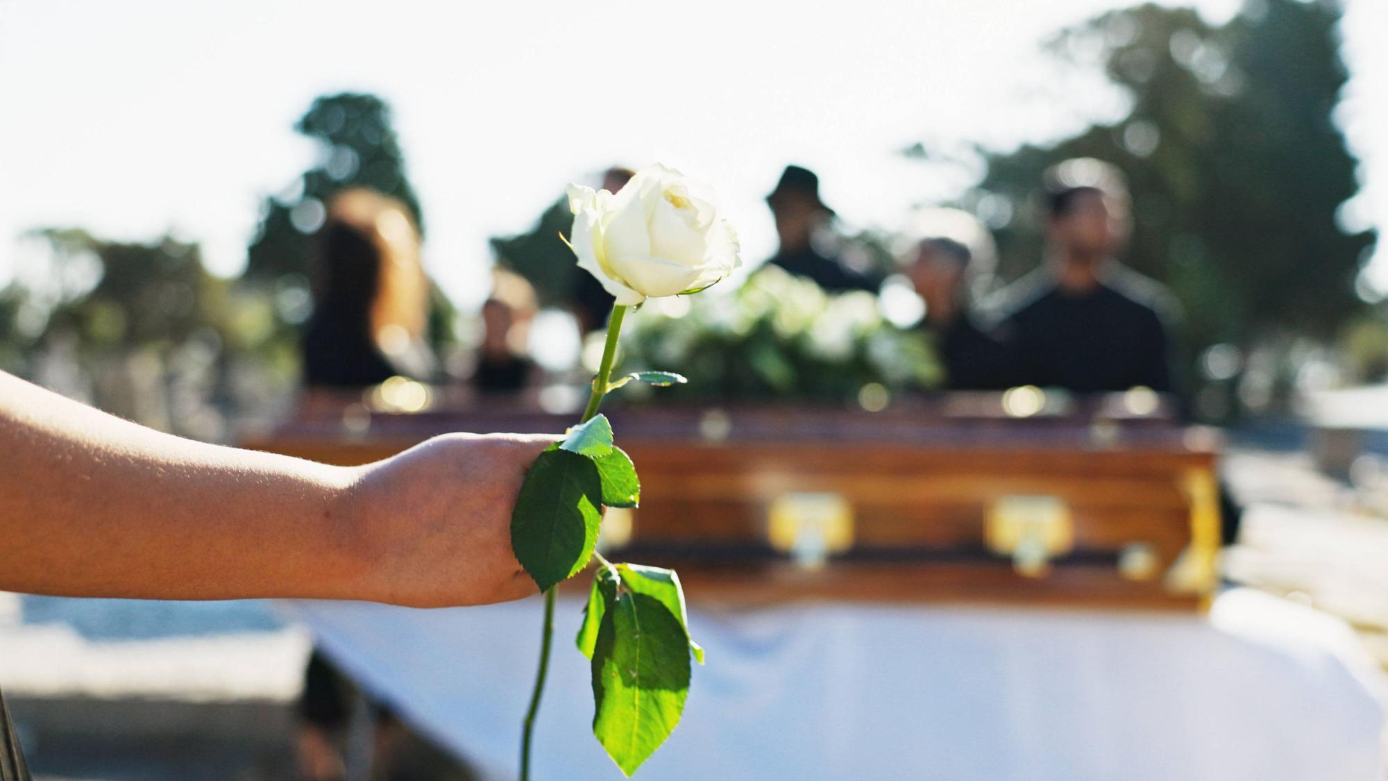 Eine Frau legt zum Andenken an eine verstorbene Person eine Blume auf einem Sarg ab. (Symbolfoto)