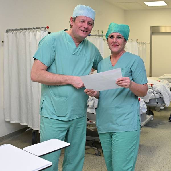 Chefarzt und OP-Managerin in OP-Kleidung stehen im Aufwachraum der Patienten und prüfen den Ausdruck für den heutigen OP-Plan.