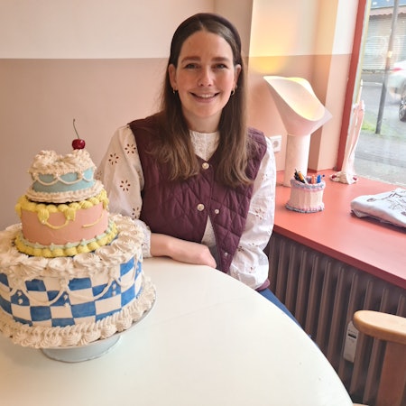 Eine junge Frau mit langem dunklem Haar sitzt an einem Tisch, auf dem ein Tortenmodell steht.