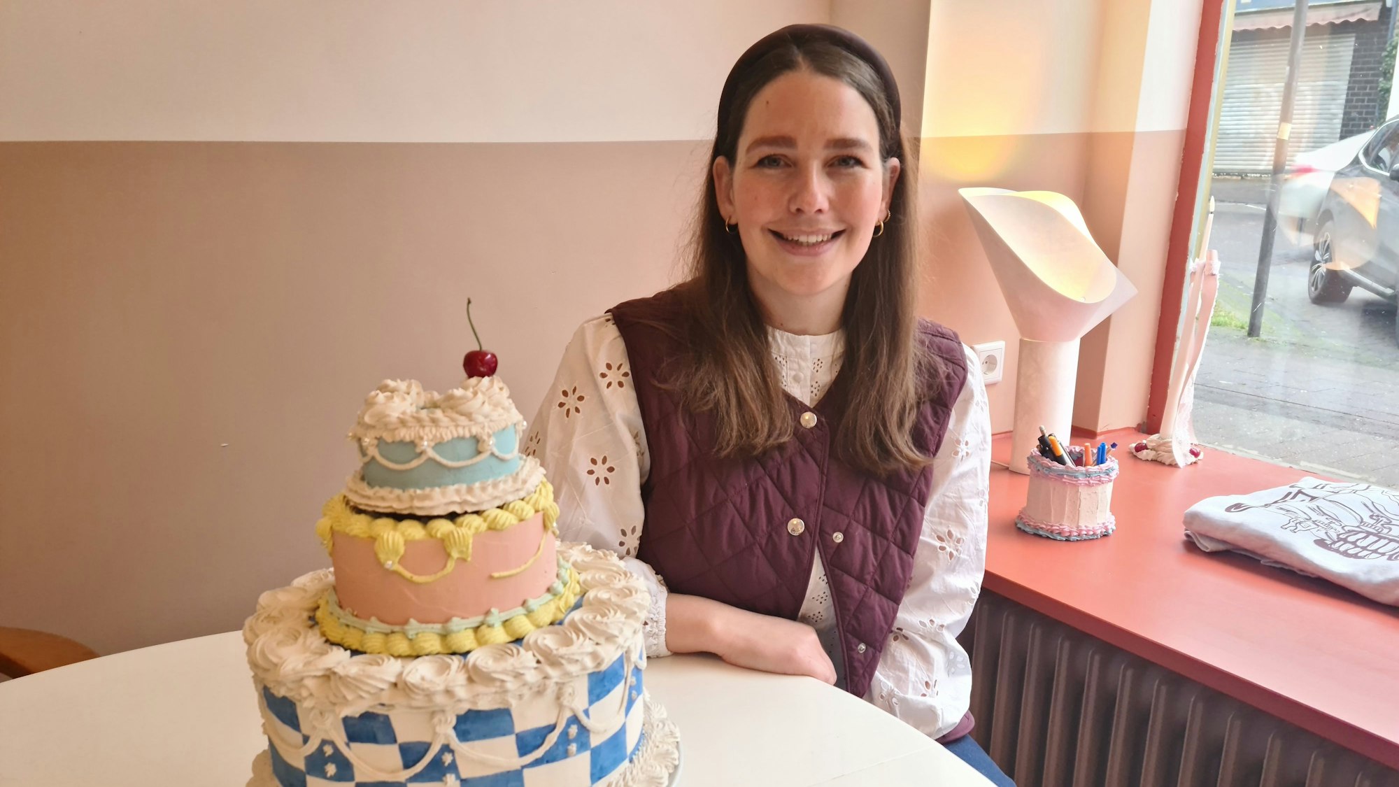 Eine junge Frau mit langem dunklem Haar sitzt an einem Tisch, auf dem ein Tortenmodell steht.