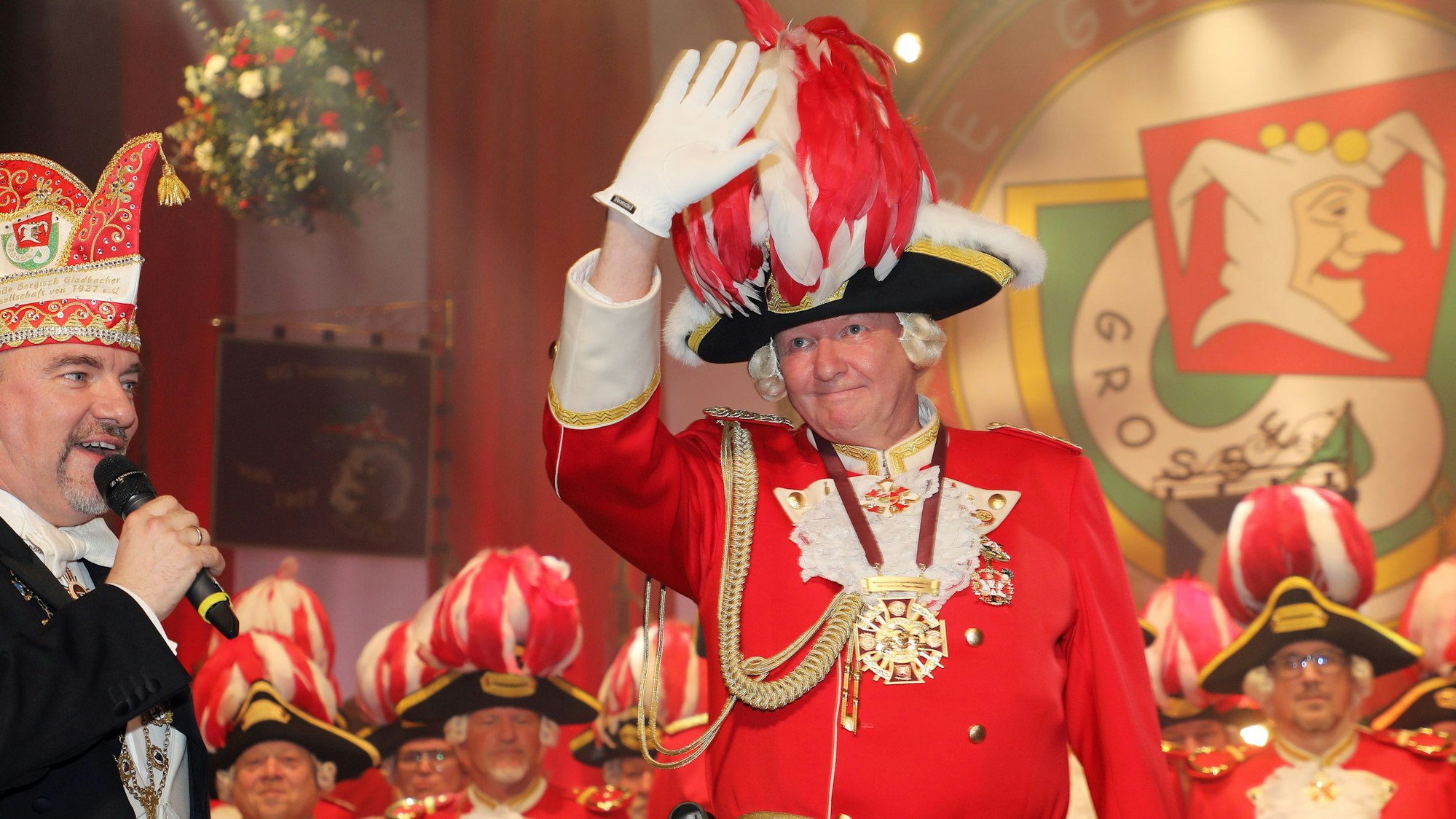 Roland Theißen winkt ins Publikum, Alexander Pfister spricht in ein Mikrofon.