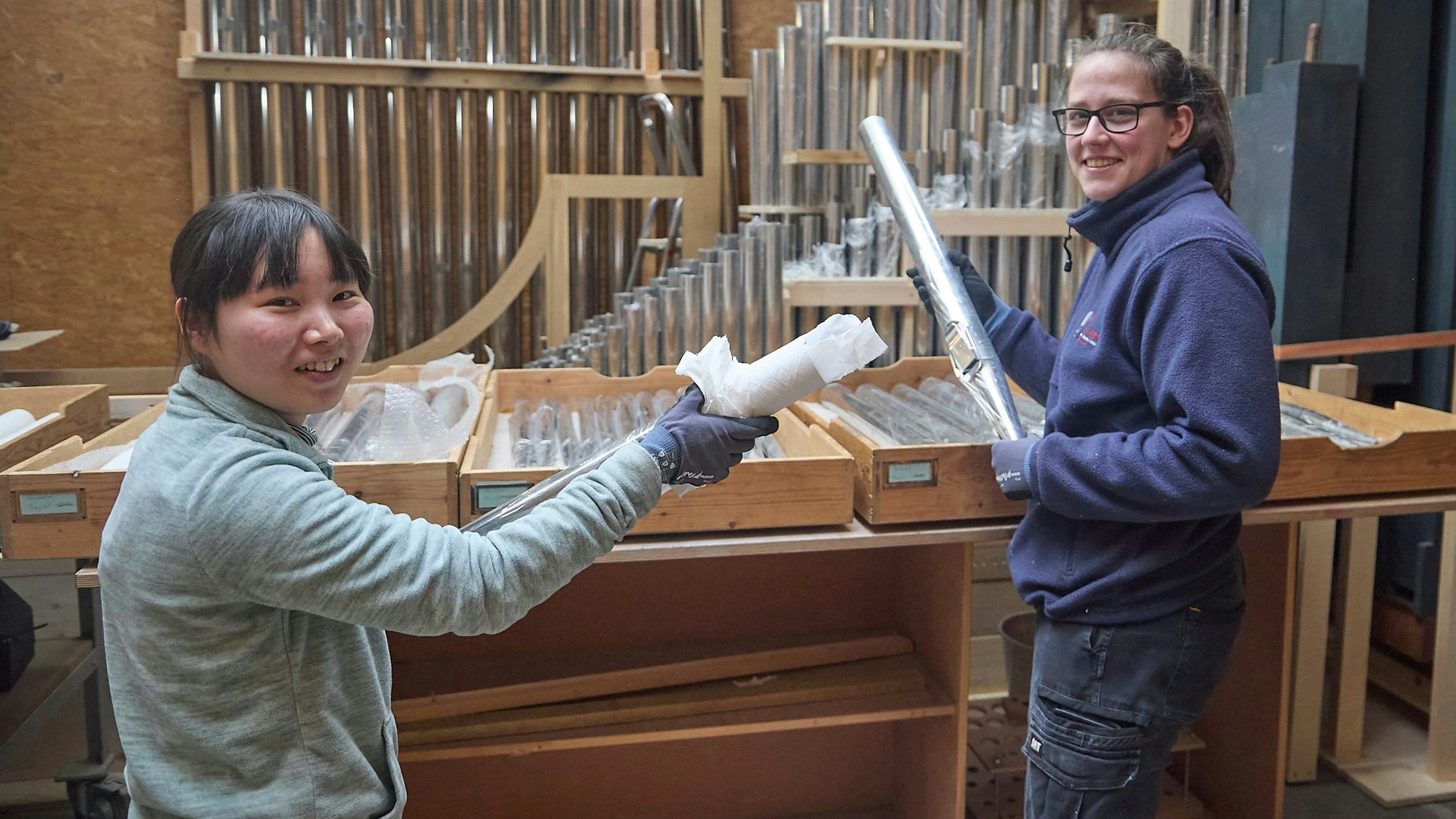 Zwei Handwerkerinnen halten Orgelpfeifen in den Händen.