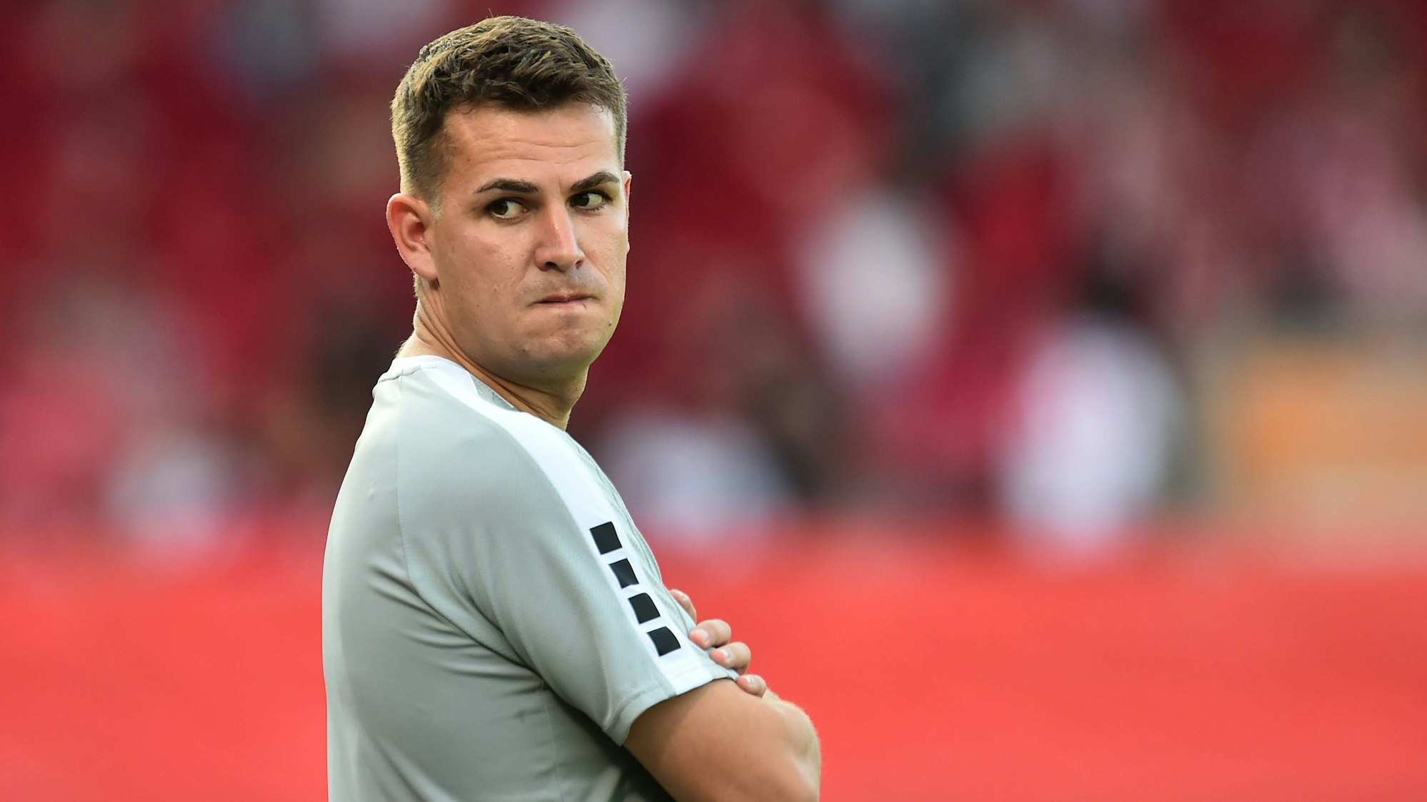 Das Foto zeigt einen Fußballtrainer mit verschränkten Armen, der über seine rechte Schulter schaut-.