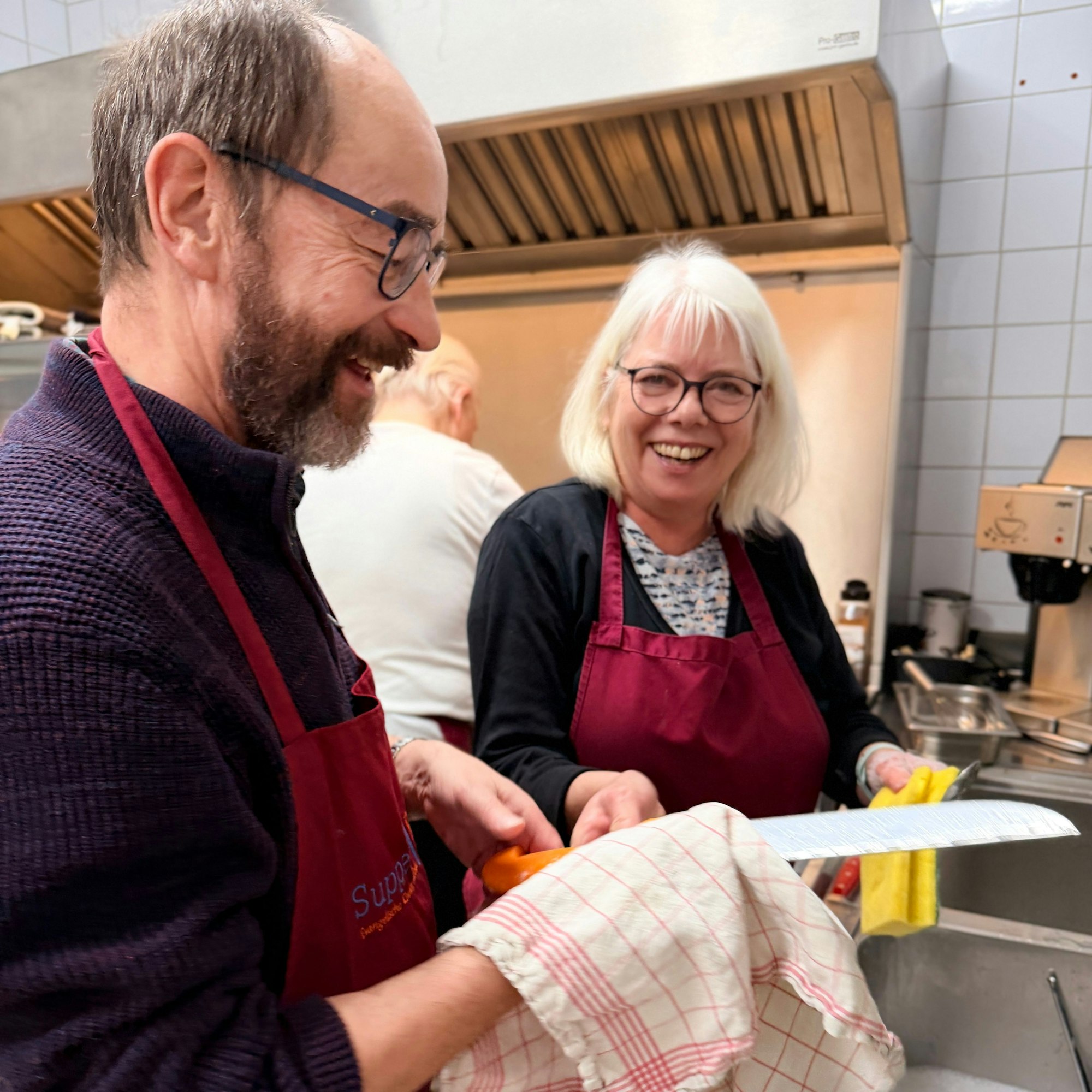 Ein Mann und eine Frau stehen an der Spüle und machen den Abwasch. Dabei sind sie sehr fröhlich und lachen.